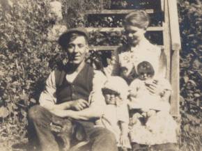 Mom standing by Grampa, with dog; Gwen on Gramma's lap